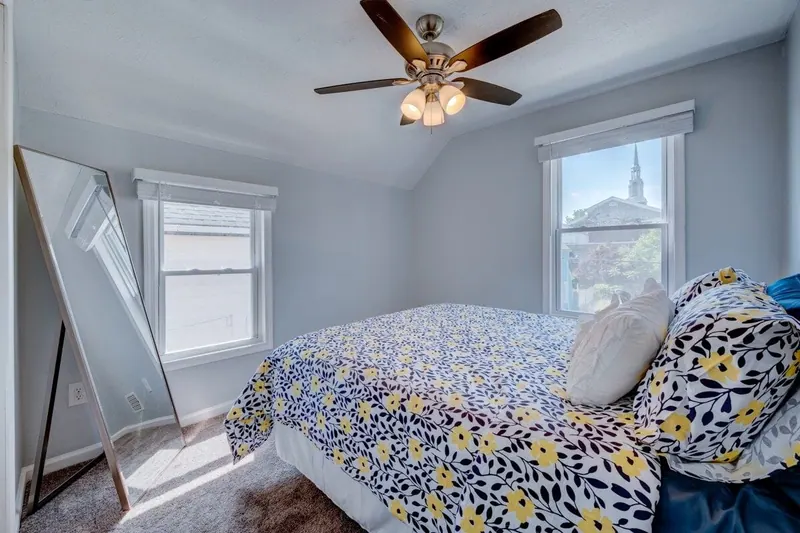 Bedroom with a full bed in floral bedding beside a bright window