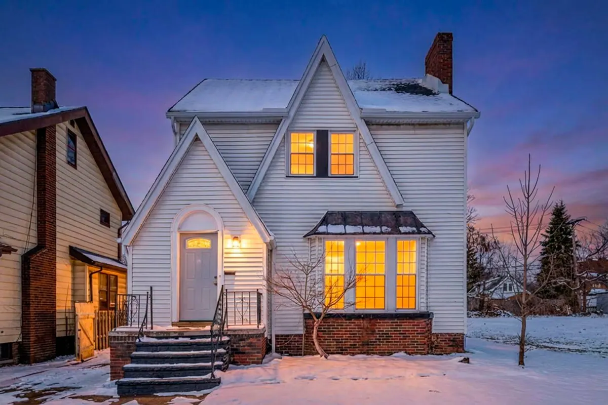 One of the homes at dusk, a white gabled house with its windows lit