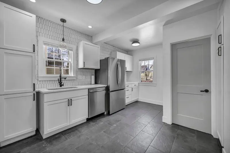 Kitchen from the hallway, with dark tile floor and white cabinets along two walls