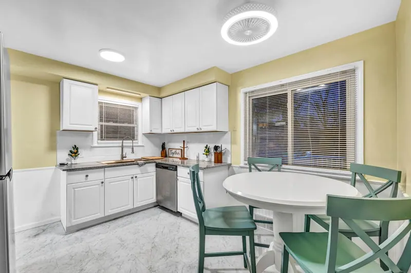 Kitchen with white cabinets, a round table and four green chairs by the window
