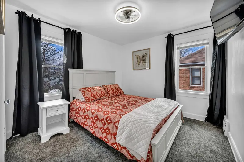 Bedroom with a pale upholstered headboard between two curtained windows