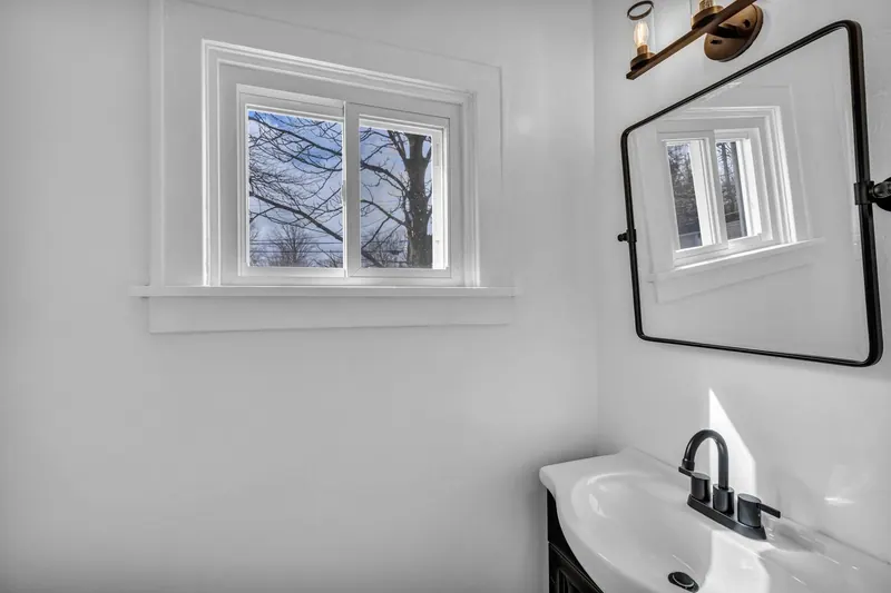 Bathroom vanity with a round mirror beside the window